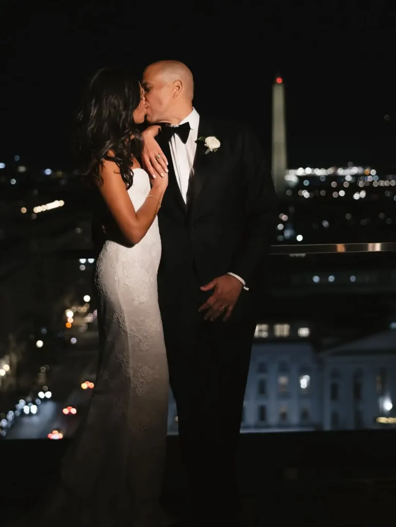 Booker kissing Lewis on the lips while she holds a bouquet of white roses and eucalyptus